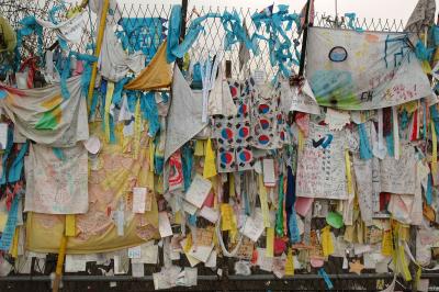 Fence at the end of the bridge festooned with t-shirts, ribbons, etc. left by visitors.